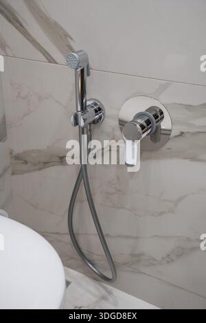 Salle de bains moderne avec douche bidet chromée et mitigeur mural sur mur carrelé de marbre Banque D'Images