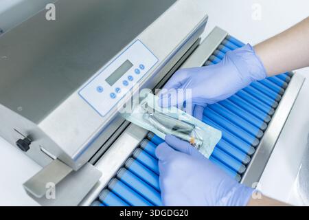 Les mains gantées scellent une poche de stérilisation avec un outil dentaire dans une clinique moderne pour le contrôle des infections et la sécurité des patients Banque D'Images