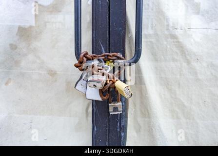 Chaîne rouillée avec plusieurs cadenas sécurisant les portes fermées des magasins, symbolisant la fermeture des entreprises, la sécurité et le déclin urbain dans un environnement urbain. Banque D'Images
