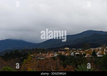 Des nuages ​​couverts planent au-dessus des maisons sur les collines et le terrain des contreforts dans un quartier de banlieue de Corona, en Californie, avec vue sur les montagnes. Banque D'Images