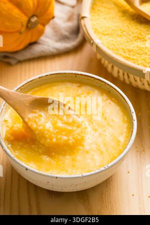 Bouillie de millet de citrouille saine dans un bol en céramique avec une cuillère en bois et de la citrouille fraîche sur la table Banque D'Images