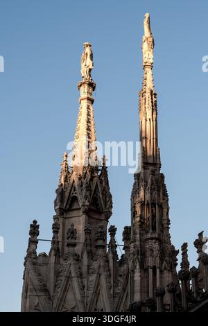 Flèches gothiques de la cathédrale de Milan à l'heure dorée contre le ciel bleu clair, architecture détaillée du Duomo di Milano et statues dans la douce lumière du soir. Banque D'Images