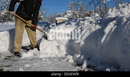 La partie inférieure d'un homme tenant une pelle en bois et dégageant une grande quantité de neige par une journée ensoleillée, le déneigement d'une zone résidentielle Banque D'Images