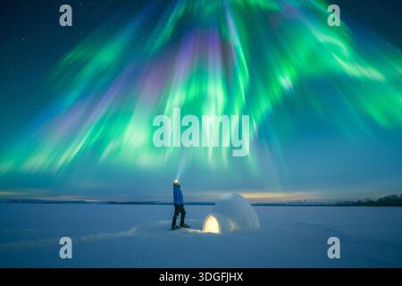 Homme avec lampe de poche près de l'igloo de neige éclairé de l'intérieur sous un ciel étoilé incroyable avec aurores boréales, paysage nocturne d'hiver, lumières polaires, aurores boréales Banque D'Images