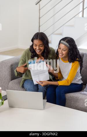 Maman diversifiée et fille adolescente assis sur le canapé dans le salon examinant le document Banque D'Images