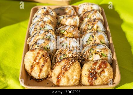 Rouleaux de sushi frits disposés soigneusement dans un plateau à emporter écologique sous la lumière du jour. Revêtement croquant, garniture au sésame et garnitures visibles highli Banque D'Images