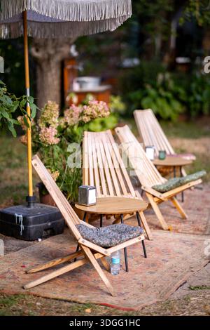 Un coin salon extérieur confortable avec chaises longues en bois avec coussins autour de petites tables rondes sous un parasol à franges, sur un tapis à motifs au milieu Banque D'Images