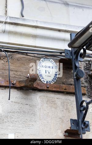 Vue rapprochée d'un panneau de permis d'alcool licence IV en émail blanc ovale attaché à une vieille poutre en bois sur une façade de bâtiment en pierre à Tours France créant Banque D'Images