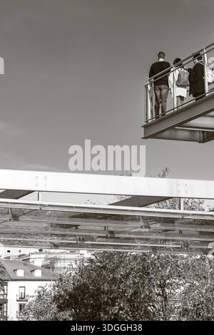 Santander, Espagne – 20 novembre 2021 : prise de vue en noir et blanc en bas angle regardant des gens debout sur la passerelle métallique du Centro Botin avec des arbres et la ville Banque D'Images