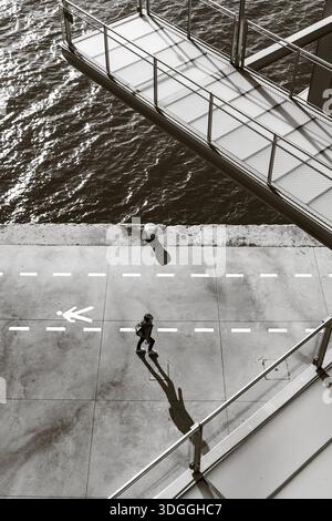 Santander, Espagne – 20 novembre 2021 : cliché noir et blanc à angle élevé d’un piéton projetant une longue ombre sur le chemin balisé sous les allées métalliques o Banque D'Images