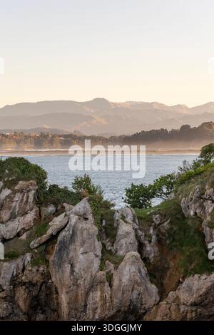 Une vue panoramique sur les falaises rocheuses de la péninsule de Magdalena à Santander, Espagne, avec la baie et les montagnes brumeuses en arrière-plan au coucher du soleil. Banque D'Images