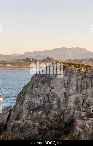 Une vue panoramique sur les falaises rocheuses de la péninsule de Magdalena à Santander, Espagne, avec la baie et les montagnes brumeuses en arrière-plan au coucher du soleil. Banque D'Images