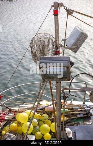 Gros plan du mât et du pont d'un bateau de pêche. L'équipement comprend des lumières de pont, un filet plongeant et un tas de bouées jaunes et de flotteurs sur le pont en dessous. Banque D'Images