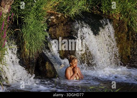 Une femme profite de l'eau sous la cascade de Ventas Rumba à Kuldiga, Kuldiga, Lettonie Banque D'Images