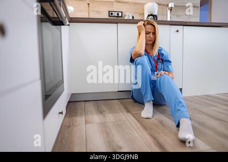 Docteur épuisé assis par terre dans la cuisine Banque D'Images