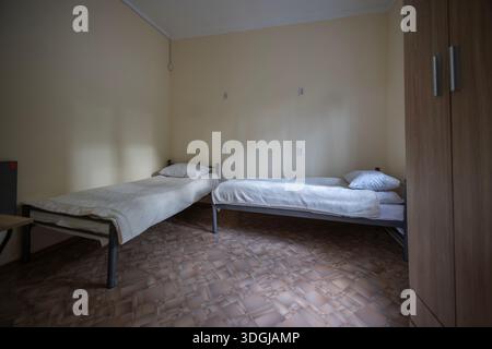 Cette chambre spartiate comprend deux lits simples, une armoire et un sol en linoléum à motifs. Cette configuration simple et fonctionnelle suggère un hébergement économique comme un h. Banque D'Images