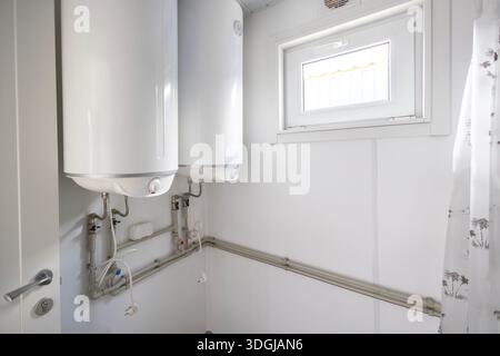 Deux grands chauffe-eau électriques sont montés sur le mur d'une buanderie fonctionnelle ou d'une salle de bains. Cette configuration assure une eau chaude suffisante pour un fac partagé Banque D'Images