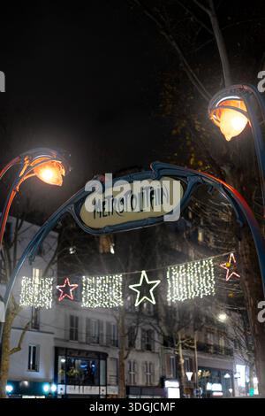 Une entrée enchanteresse Art Nouveau 'Metropolitain' à Paris la nuit. Les deux lampes emblématiques brillent chaleureusement au milieu des lumières de Noël festives en forme d'étoile, cre Banque D'Images
