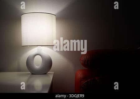 Lampe Moody projetant des ombres profondes, ambiance sombre avec silhouette de canapé rouge et lueur chaude concentrée, dramatique Banque D'Images