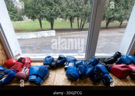 Une section de formation en boxe dans une communauté rurale avec des ressources limitées. Plusieurs paires de gants de boxe en rouge, bleu et noir reposent sur une surface en bois Banque D'Images