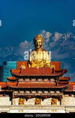 Statue de Bouddha doré dans un temple de montagne dans le Xinjiang, Chine, avec des sommets enneigés des montagnes Tianshan s'élevant en arrière-plan. Banque D'Images