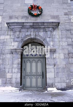 Une porte arquée décorative d'une église en pierre à Ottawa est ornée d'une couronne de Noël un jour neigeux de janvier Banque D'Images