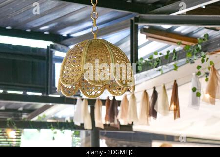 Lampe en rotin tissé avec bords festonnés suspendue dans un espace extérieur confortable décoré de vignes. Banque D'Images