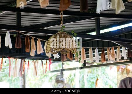 Lampe en rotin tissé avec bords festonnés suspendue dans un espace extérieur confortable décoré de vignes. Banque D'Images