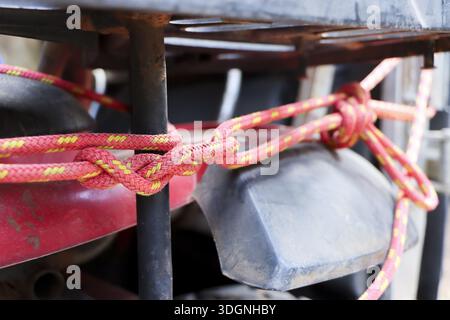 Gros plan de détail d'une corde en nylon rouge solide avec fil jaune noué dans un nœud serré sécurisé autour de la barre en acier rouillé du camion montrant robuste durable et s. Banque D'Images