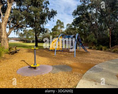 Une aire de jeux contemporaine pour enfants dotée d'une structure d'escalade colorée avec des filets, un banc en bois et un paillis de sécurité, située dans un parc ensoleillé. Banque D'Images
