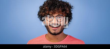 Jeune homme sourit largement sur un fond bleu pendant un moment joyeux Banque D'Images