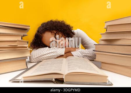 Étudiant Studies Hard et Falls endormis au bureau entouré de livres dans la salle jaune vif Banque D'Images