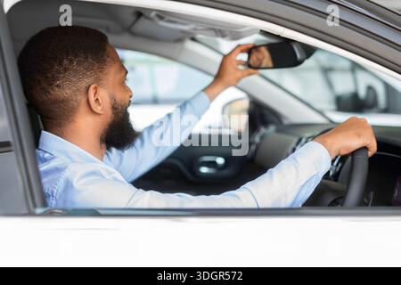 Jeune homme noir assis à l'intérieur de la voiture et ajustant le rétroviseur Banque D'Images