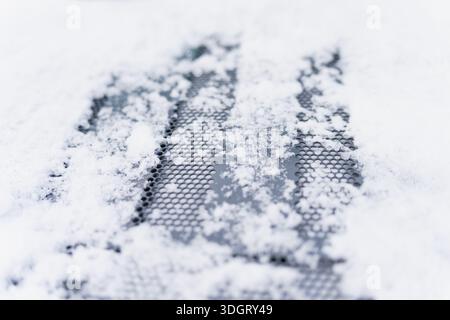 Grille métallique perforée recouverte de neige en vue macro, texture hivernale douce avec cristaux de glace dispersés formant un motif abstrait sur une surface sombre Banque D'Images
