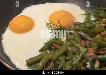 Oeufs frits avec mélange de légumes haricots verts champignons et herbes cuisant dans une poêle Banque D'Images