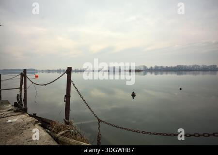 Chaîne de fer sur un coin par le bord d'une jetée au bord du lac, avec des bouées flottantes à proximité et un ciel nuageux coulé dans l'eau, dans le pays italien Banque D'Images