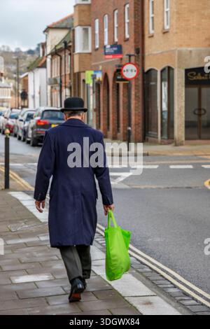 Habille intelligemment l'homme plus âgé portant chapeau Bowler et portant sac en plastique vert marchant seul le long d'une rue du centre-ville. Banque D'Images