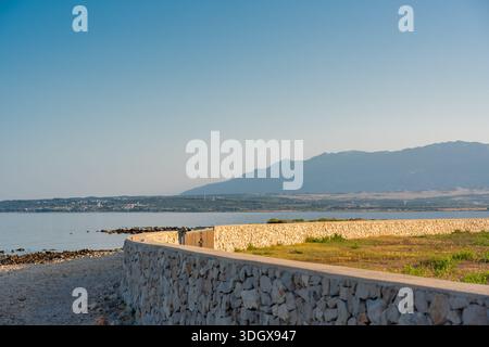 Terrain côtier pour maison près de la mer calme avec clôture en pierre et vue sur la montagne sous ciel bleu clair. Concept immobilier, propriété balnéaire, bâtiment lan Banque D'Images