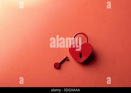 Cadenas en forme de coeur rouge avec clé sur fond coloré chaud avec espace de copie. Concept Saint-Valentin, carte de voeux. Banque D'Images