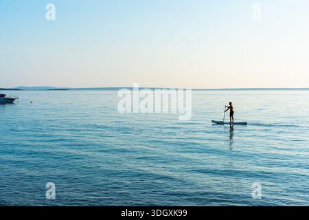 Homme debout sur paddleboard au milieu de la mer bleue calme sous ciel clair. Concept de style de vie actif, sports nautiques, sup surf, solitude avec natu Banque D'Images