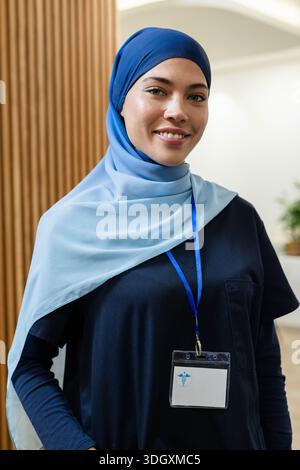 Infirmière souriante à la réception, portant un foulard et des gommages bleu marine avec badge d'identification transparent sur la longe Banque D'Images