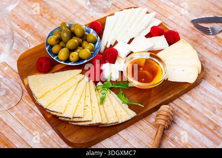 Différents types de fromage, miel, framboises et olives sur bois Banque D'Images