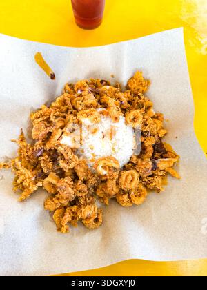 Service de Nasi Lemak Sotong Goreng sur papier parchemin, fond de table jaune vif. Banque D'Images