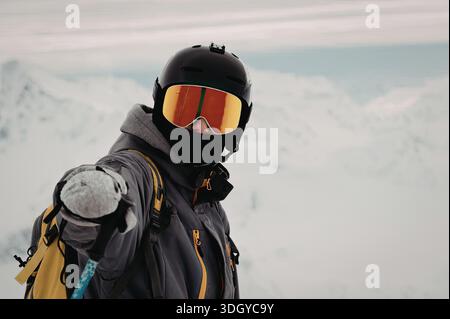Un snowboarder se tient dans un paysage montagneux enneigé, portant un équipement de protection et tenant un snowboard. Banque D'Images
