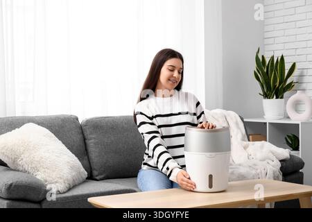 Jeune femme assise sur un canapé noir et allumant l'humidificateur moderne dans le salon Banque D'Images