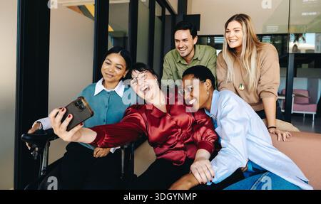 Une équipe de jeunes professionnels énergiques souriant ensemble tout en capturant un selfie. La photo respire la joie, la collaboration et la diversité, mettant en valeur pos Banque D'Images