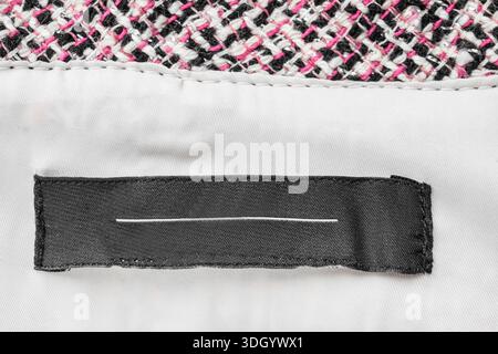 Étiquette de vêtements noirs vide cousue sur fond de tissu blanc dessous gros plan Banque D'Images