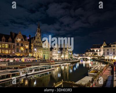 Les lumières de Noël illuminent le front de mer historique de la rivière Leie de Gand la nuit, reflétant les couleurs festives chaudes sur l'eau pendant que les bateaux passent à travers Banque D'Images