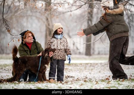 mère et filles de différents âges jouent avec le chien dans le parc enneigé Banque D'Images