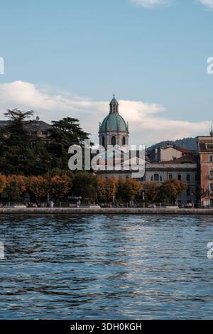 Le majestueux dôme de la cathédrale de Côme (Duomo di Como) vu du lac, entouré d'une architecture historique et d'arbres luxuriants en Lombardie, Italie. Banque D'Images